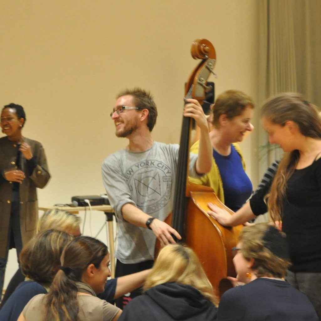 Doug Kemp playing double bass in a crowd, smiling