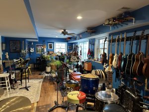 Kim McCord's incredible basement studio. Loads of guitars on the walls, Drum kits and instruments everywhere in a mid blue room. 