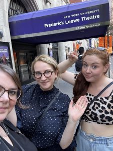 Emma, Caitlin and Rebecca outside NYU with Rebecca pointing at the sign