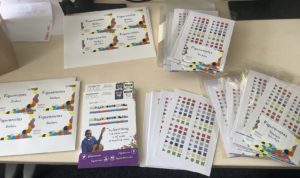 Colourful Figurenotes stickers on a table. Some are in cellophane packets. Also on the table are Figurenotes flyers and labels for the packs ready to package up. 