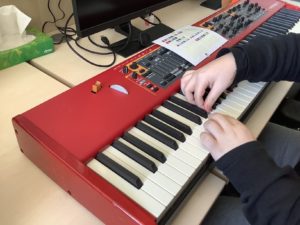 Image shows two hands and Figurenotes stickers being placed onto a keyboard manually. The keyboard is red. 