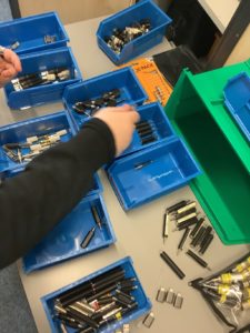 Several blue plastic boxes are on a table. A pair of hands is showing sorting different adapters into their relevant boxes. 