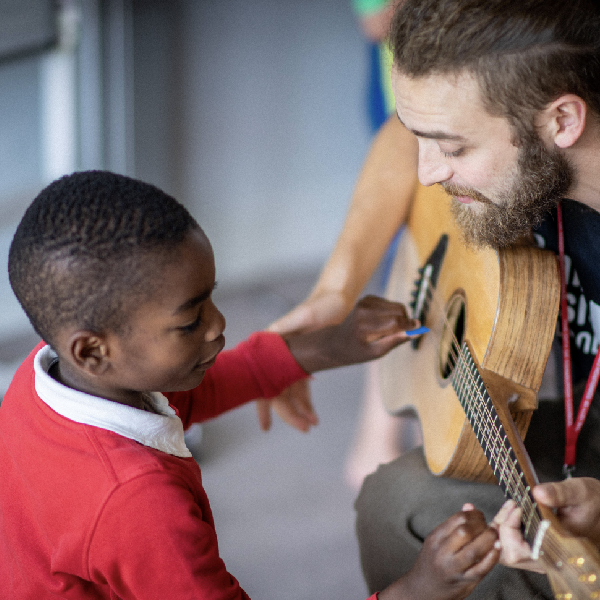 A boy gently plays a Gazouki held by Associate Musician Tenzin Stephen.