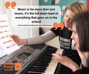 "Music is far more than just music, it's the full heart beat of everything that goes on in the school" - Graeme Boyd Headteacher, Carronhill School. This text is sitting in a rectangle with large orange quote marks. The main body of the image is DMS Musician Abi Sinar with light brown hair and smiling, wearing black DMS T-shirt and white striped top underneath holding Figurenotes sheet music up for a girl with dark hair playing the tune on a keyboard and smiling.